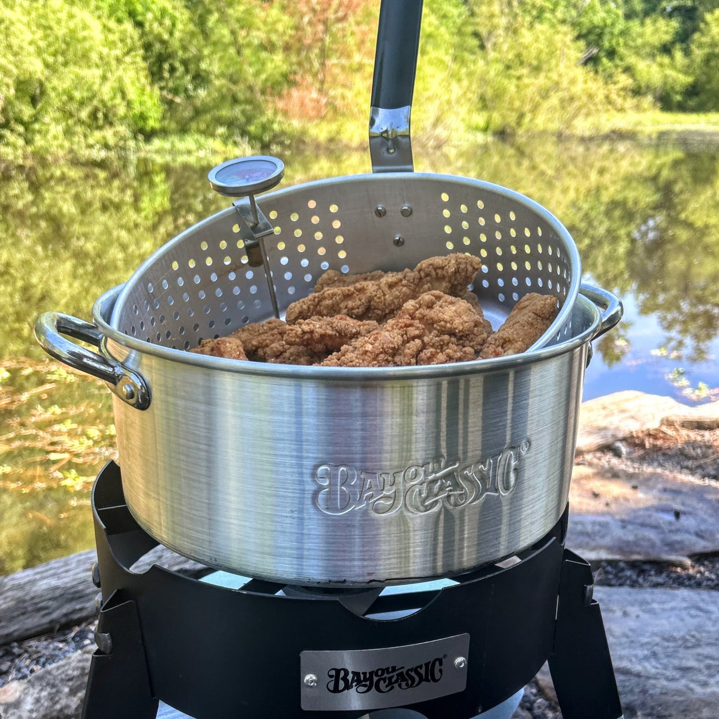 Fry pot with fried chicken on an outdoor cooker by a lake