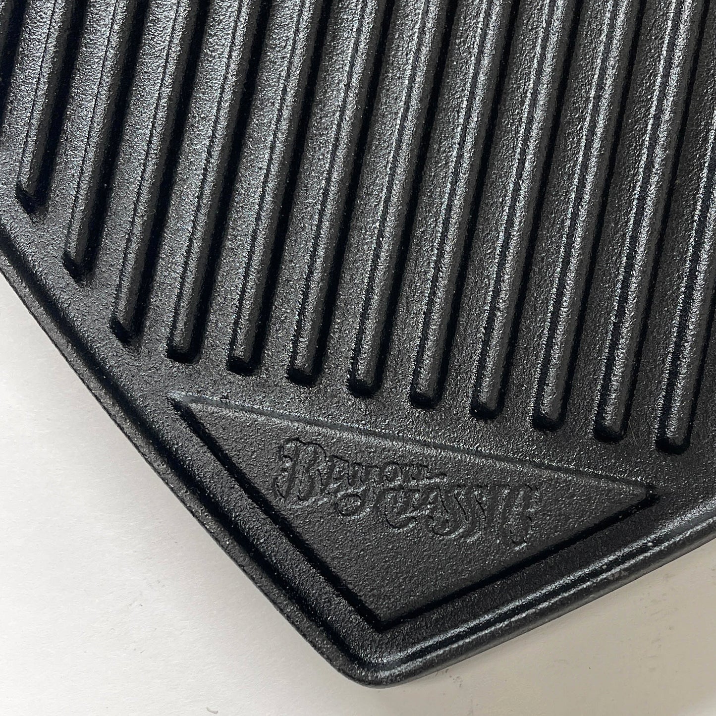 Close up of the ribbed side of a cast iron griddle on a white background.