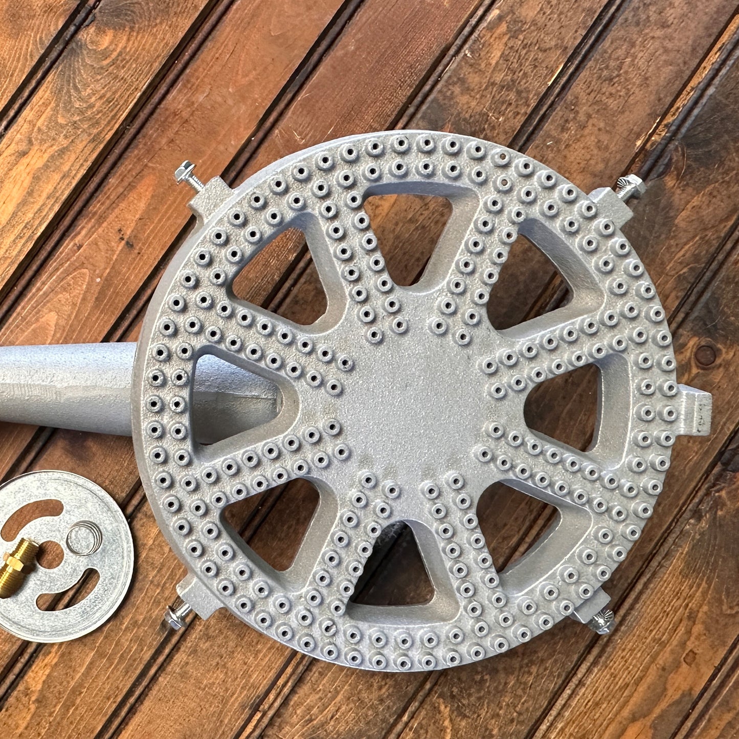 Cast iron banjo burner with orifice, air shutter, and spring on a wood surface.