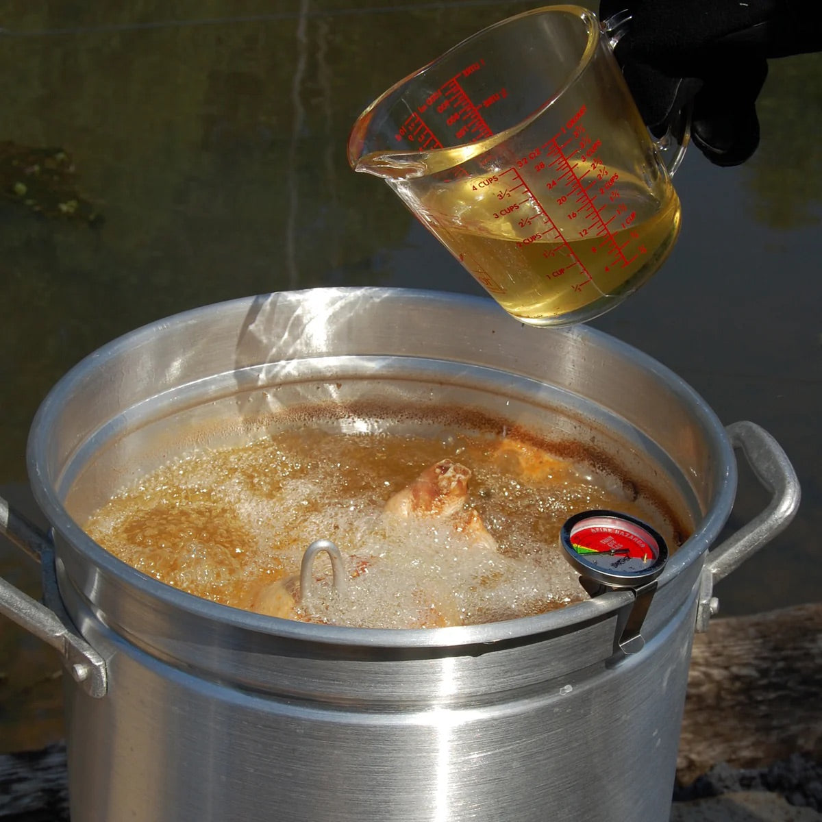 Measuring cup pouring liquid into a turkey fryer that is frying a turkey outside