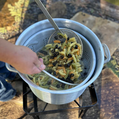 Pasta being drained in an aluminum basket over a pot outdoors