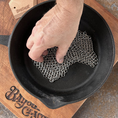 Person using chainmail scrubber in a cast iron skillet