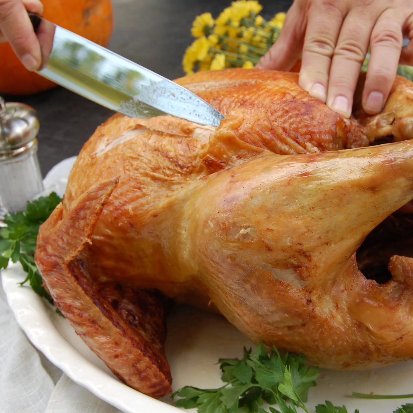 Hands holding a knife beginning to carve a turkey on a platter