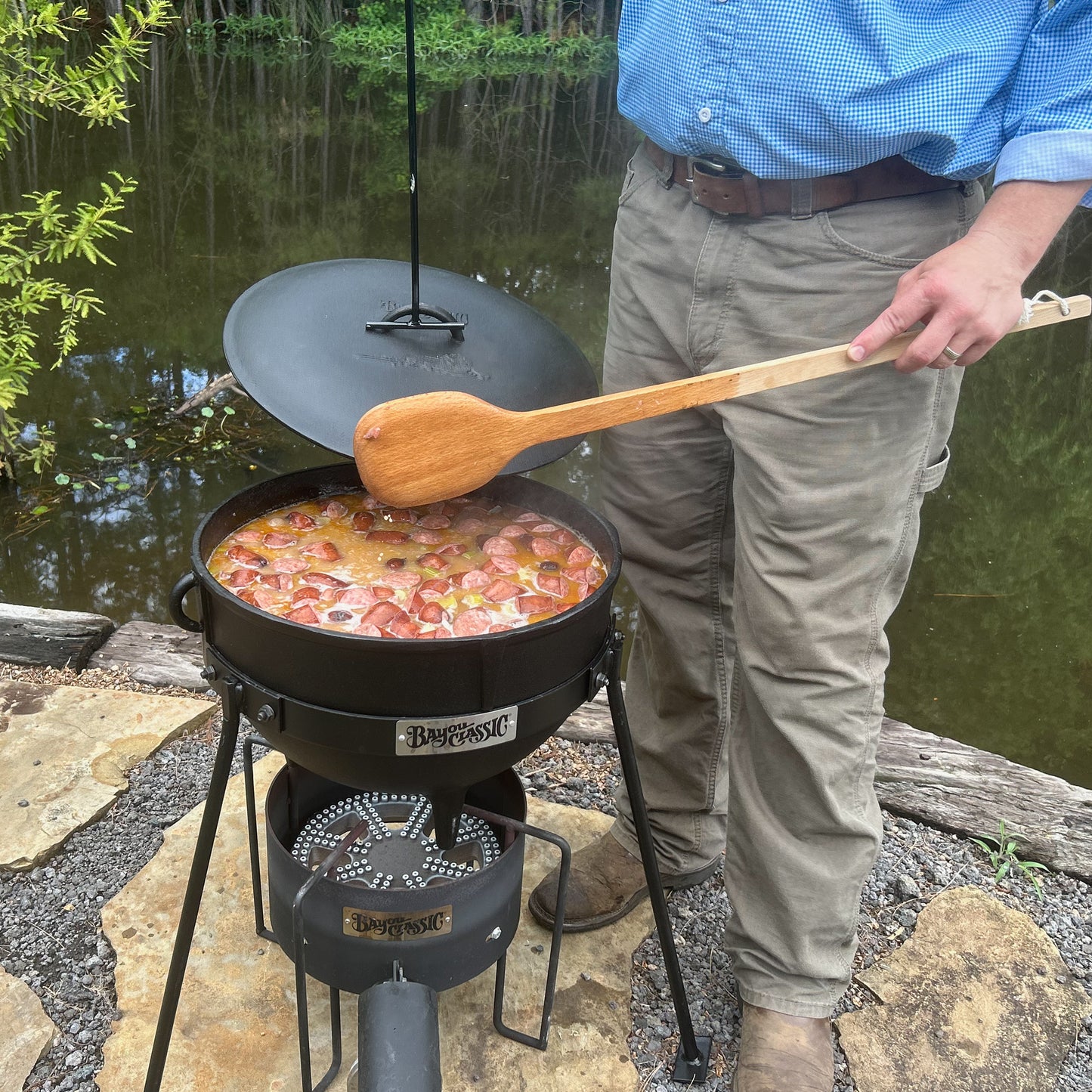 Person cooking outdoors using a cast iron jambalaya kettle and stand over an outdoor cooker 