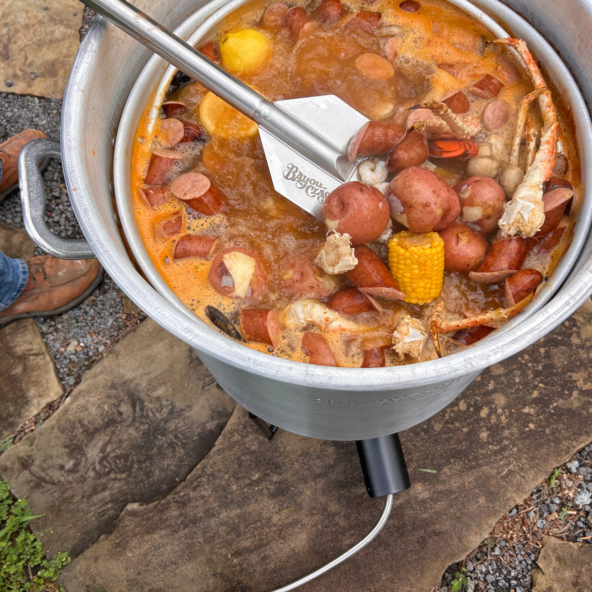 Low country boil with crab legs and vegetables using a stir paddle in an aluminum stockpot