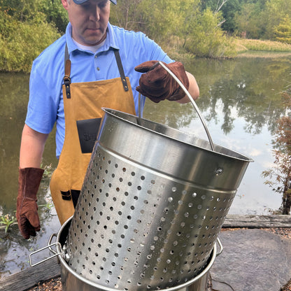 Person lifting a stainless steel basket out of a stockpot by a body of water