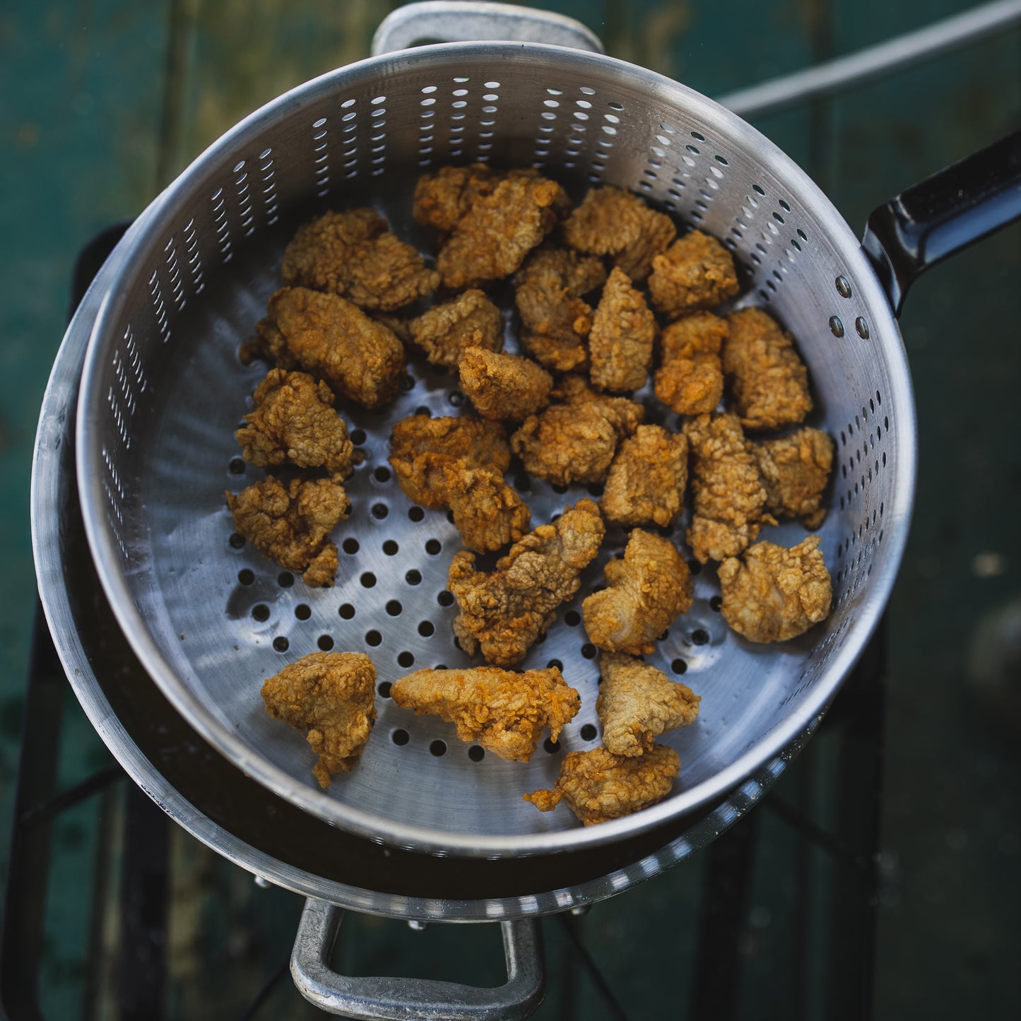 Fried chicken pieces in an aluminum fry pot on an outdoor cooker