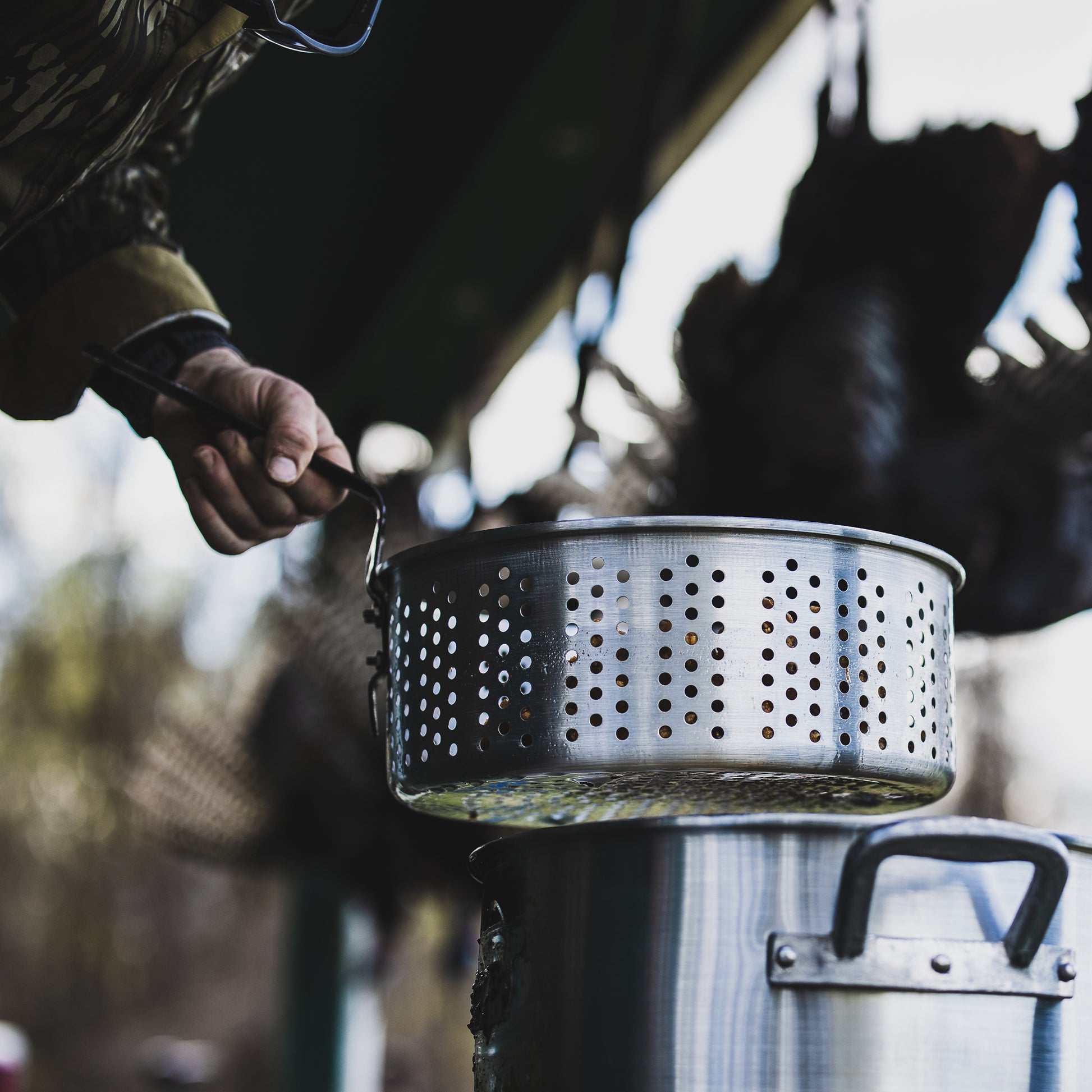Person using a perforated fry basket over a pot outdoors