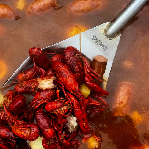 Boiled crawfish in a pot with a large spoon, surrounded by a blurred background of more crawfish.