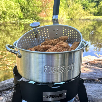 Fry pot with fried chicken on an outdoor cooker by a lake