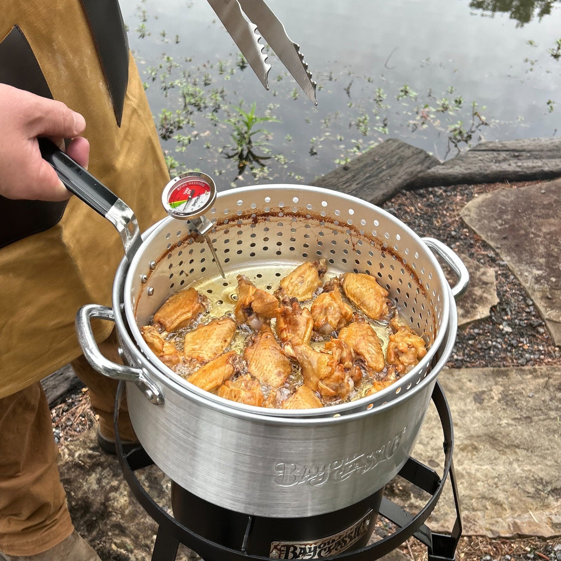 Man frying  chicken wings in a fry pot over a single burner