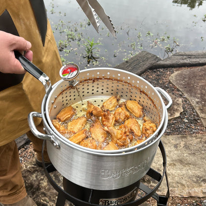 Man frying  chicken wings in a fry pot over a single burner