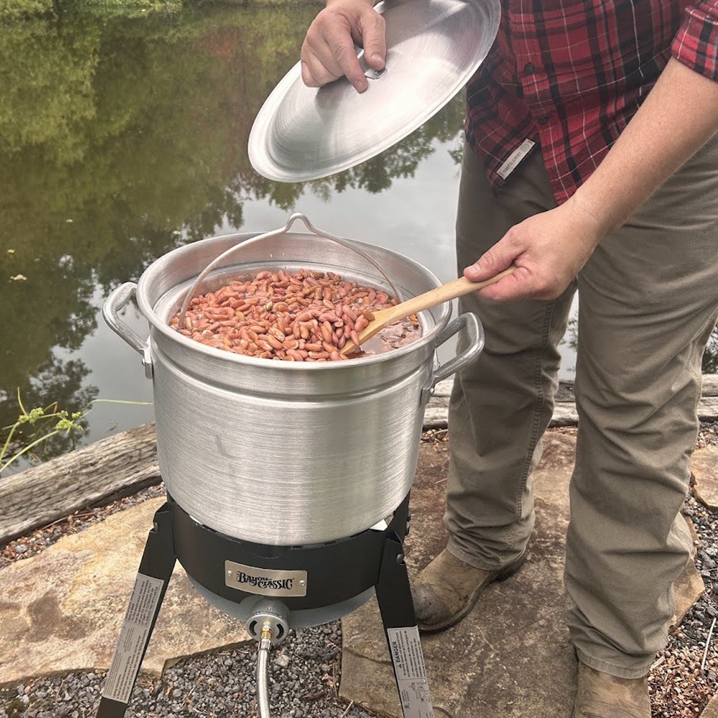Person cooking beans outdoors using an aluminum stockpot with basket and an outdoor cooker