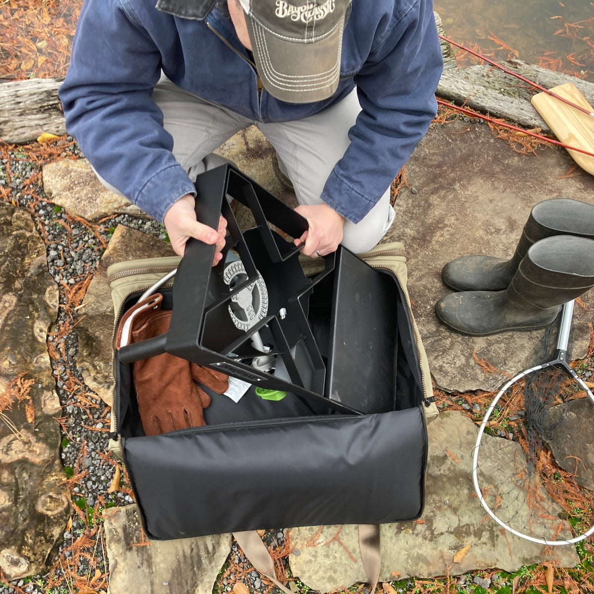 Man removing an outdoor cooker from a gear bag next to mud boots and a net