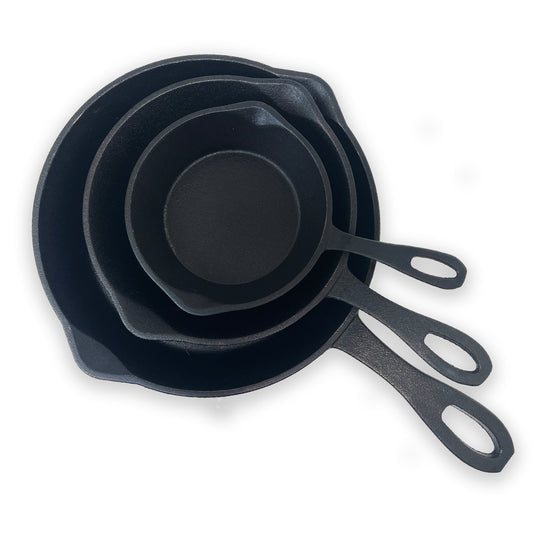 A set of three black cast iron skillets, stacked from largest to smallest, with pour spouts and handles on a white background.