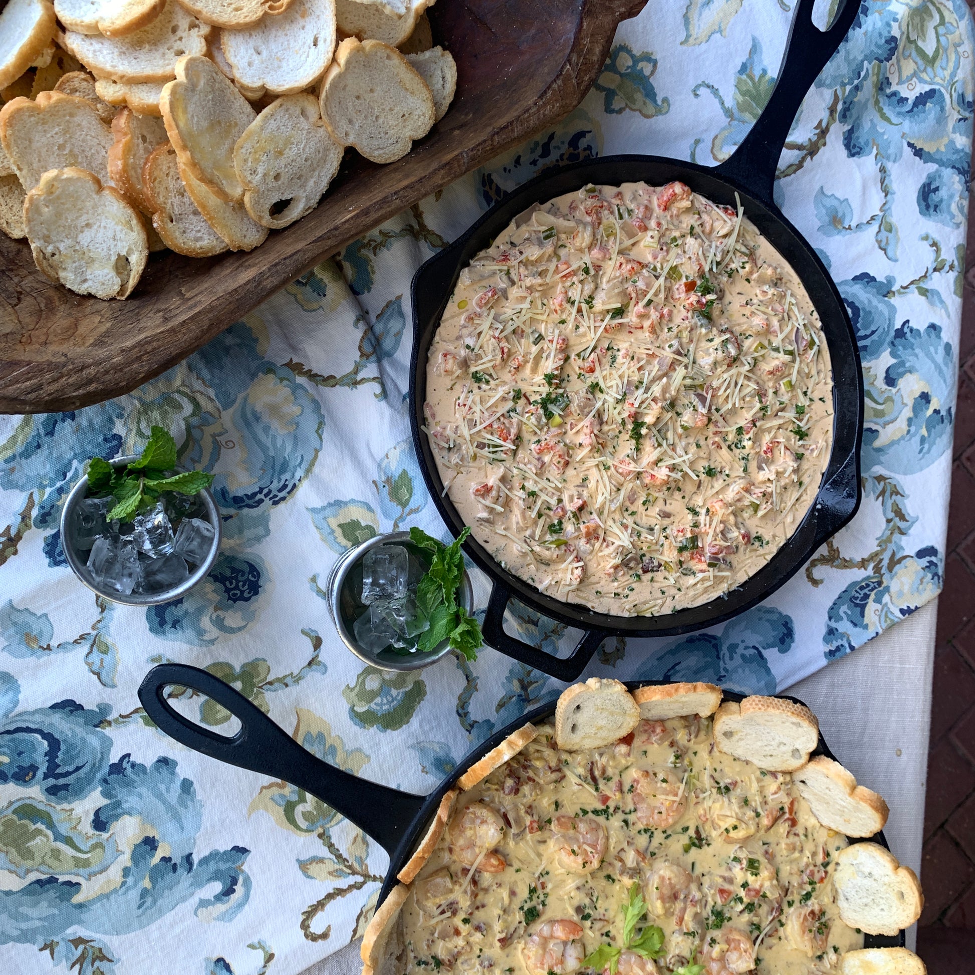 Two cast iron skillets with crawfish cheese dip on a table with a floral tablecloth.
