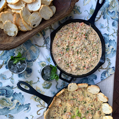 Two cast iron skillets with crawfish cheese dip on a table with a floral tablecloth.