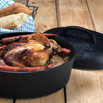 Cast Iron Oval Roaster with roasted chicken and carrots on a wooden surface