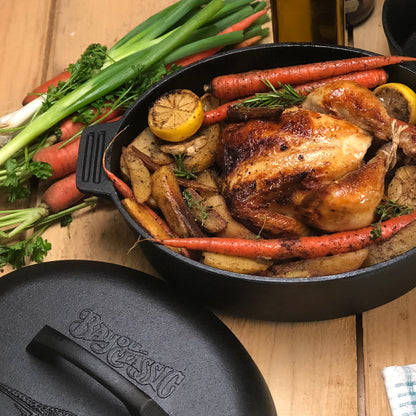 Cast Iron Oval Roaster with roasted chicken and vegetables on a wooden surface