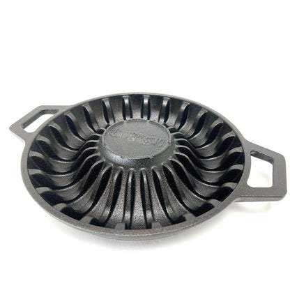 A black cast iron shrimp pan with ridged pattern to hold shrimp and two handles on a white background