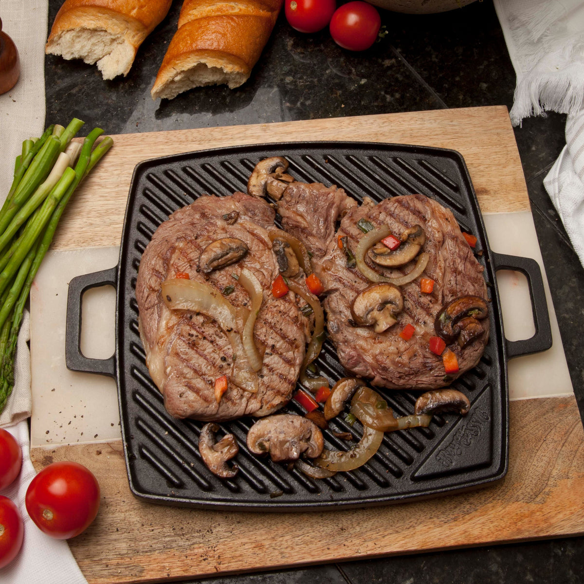 Black cast iron griddle with steaks on a table with vegetables