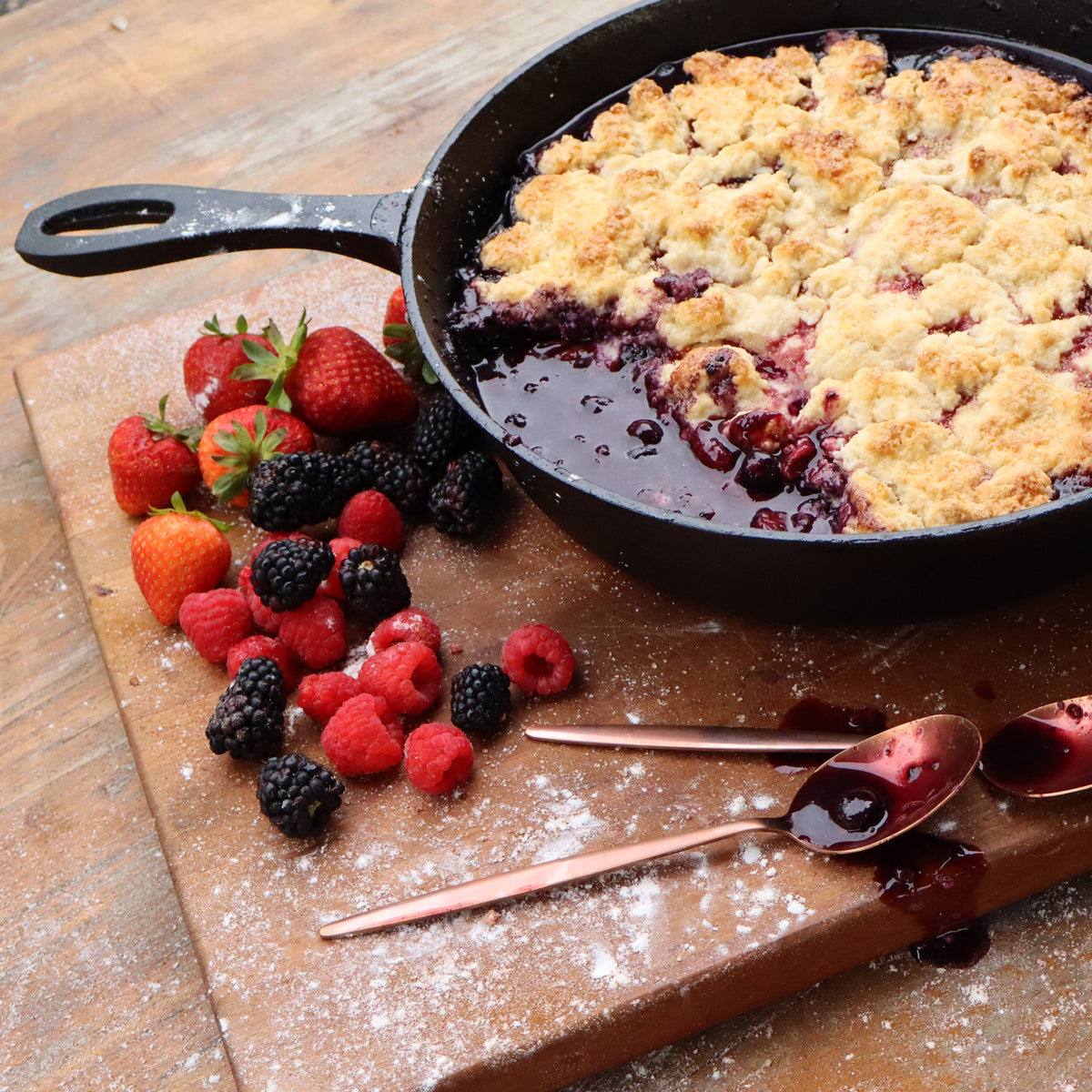 Cast Iron Skillet with berry cobbler and two spoons next to it