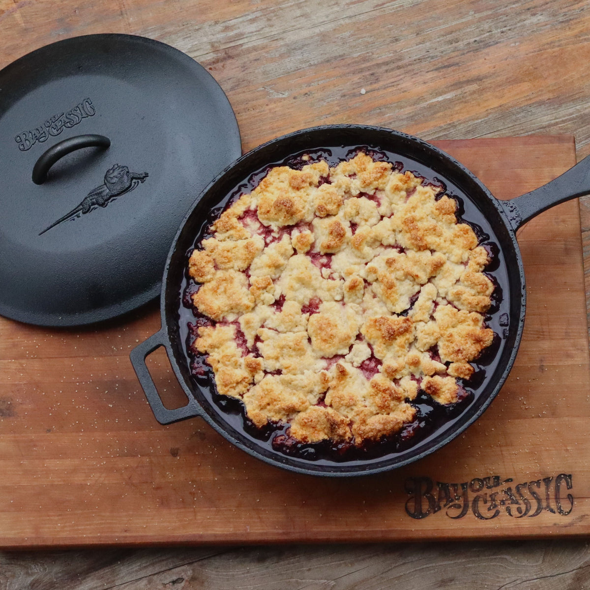 Berry cobbler in a cast iron skillet with lid on a wood table