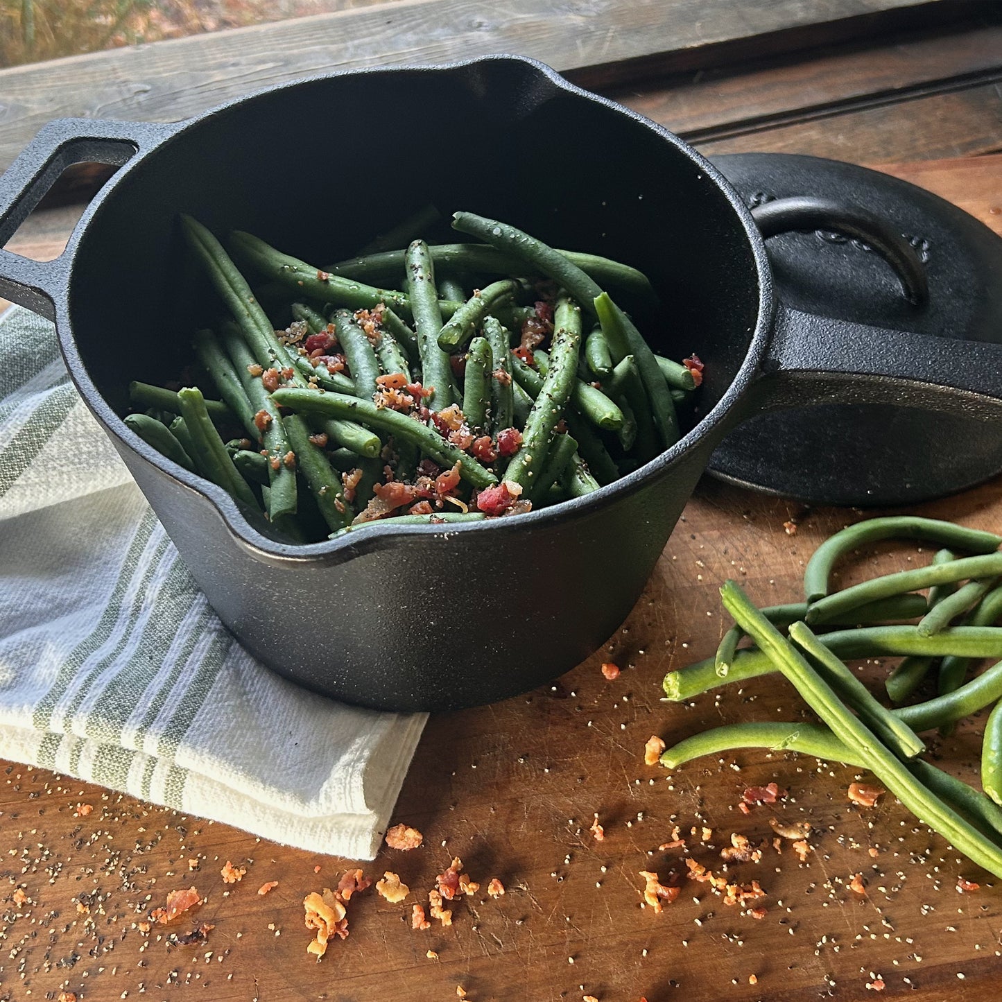 Black cast iron pot with green beans and bacon on a wooden surface