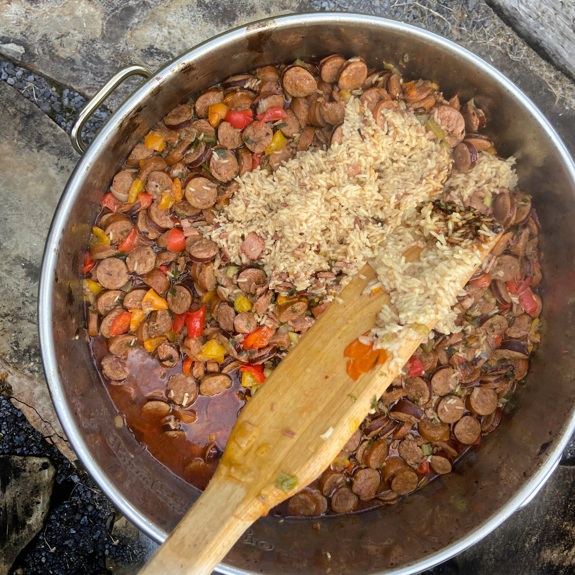 Overview image of stainless kettle with cooked sausage and rice and a wooden stir paddle