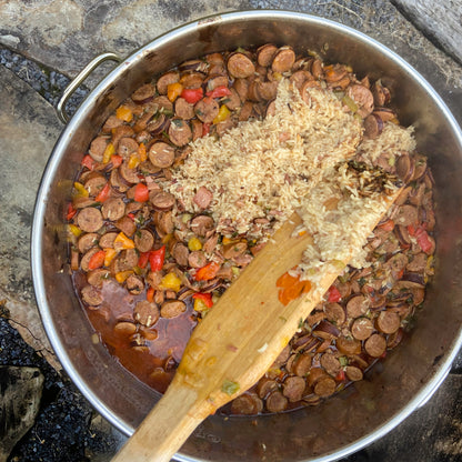 Overview image of stainless kettle with cooked sausage and rice and a wooden stir paddle