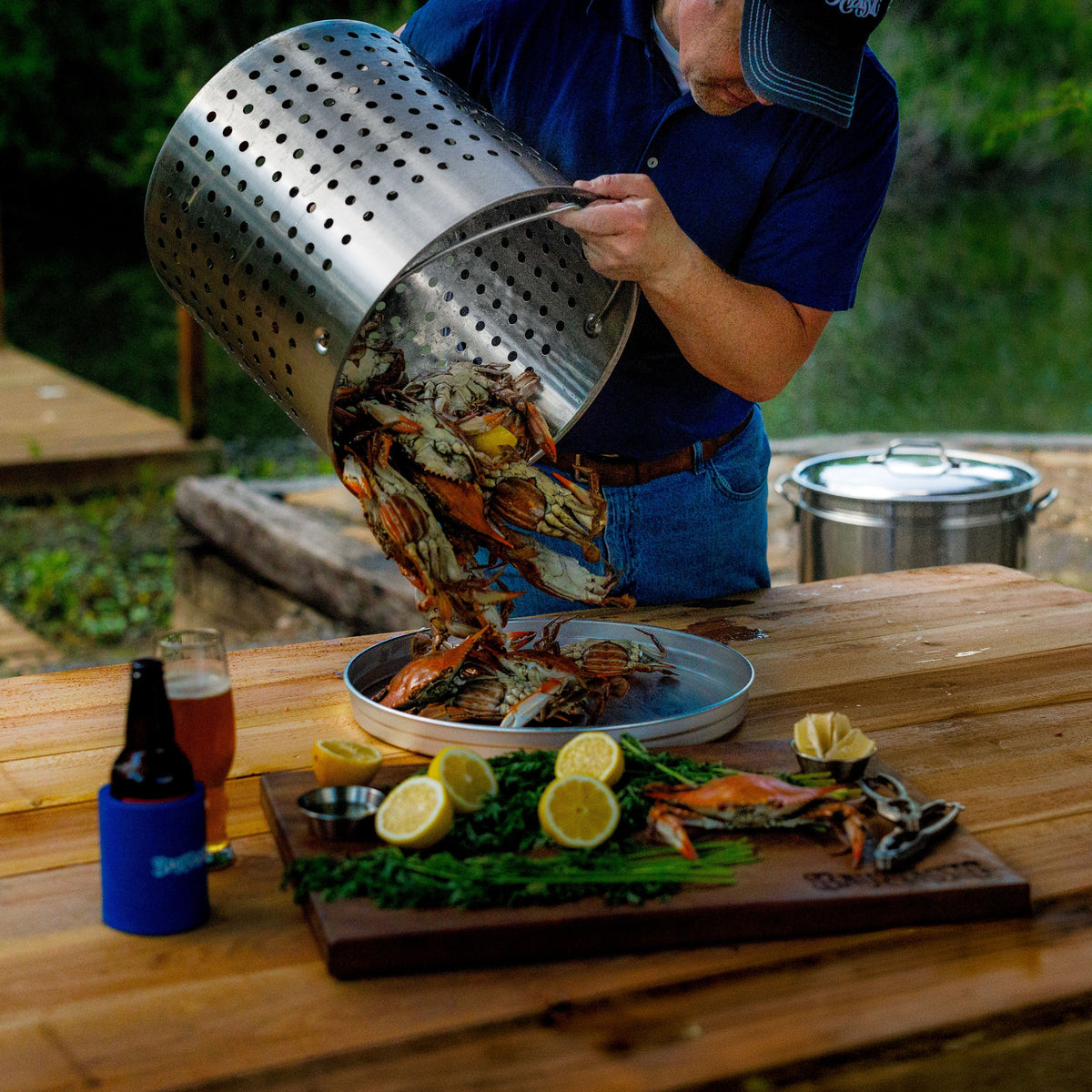 Person serving boiled crabs from a stockpot basket onto a plate on a wooden table outdoors.