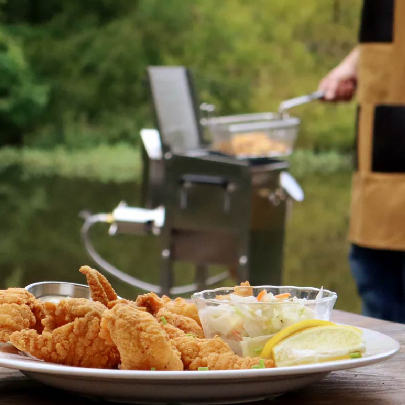 Fried chicken on a plate with coleslaw and pickles, grill in the background