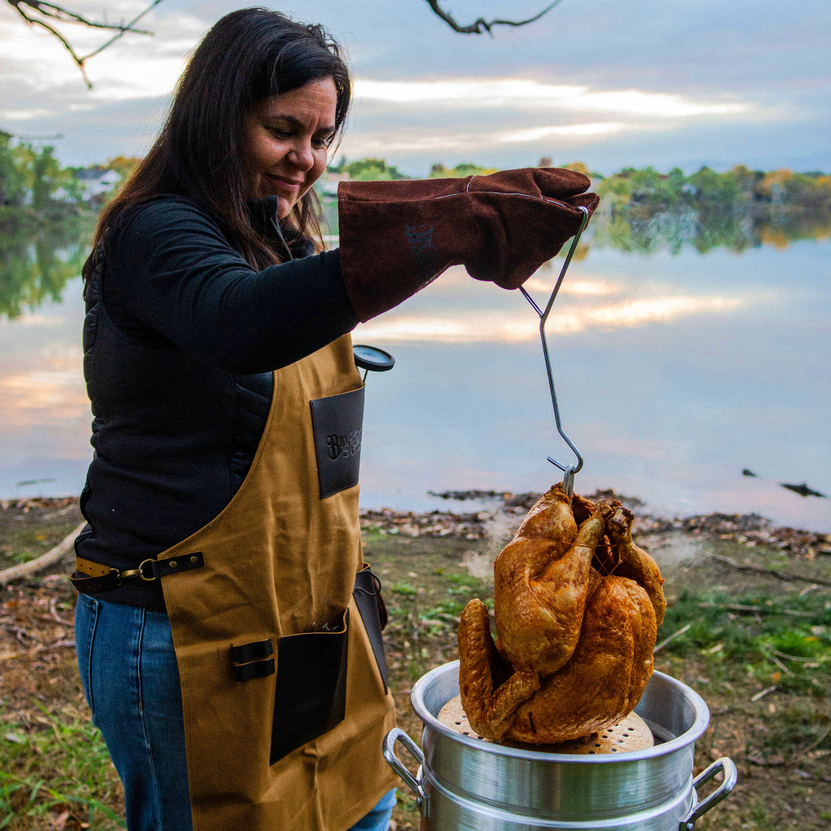 Lady frying a turkey in an aluminum turkey fryer outside by a lake