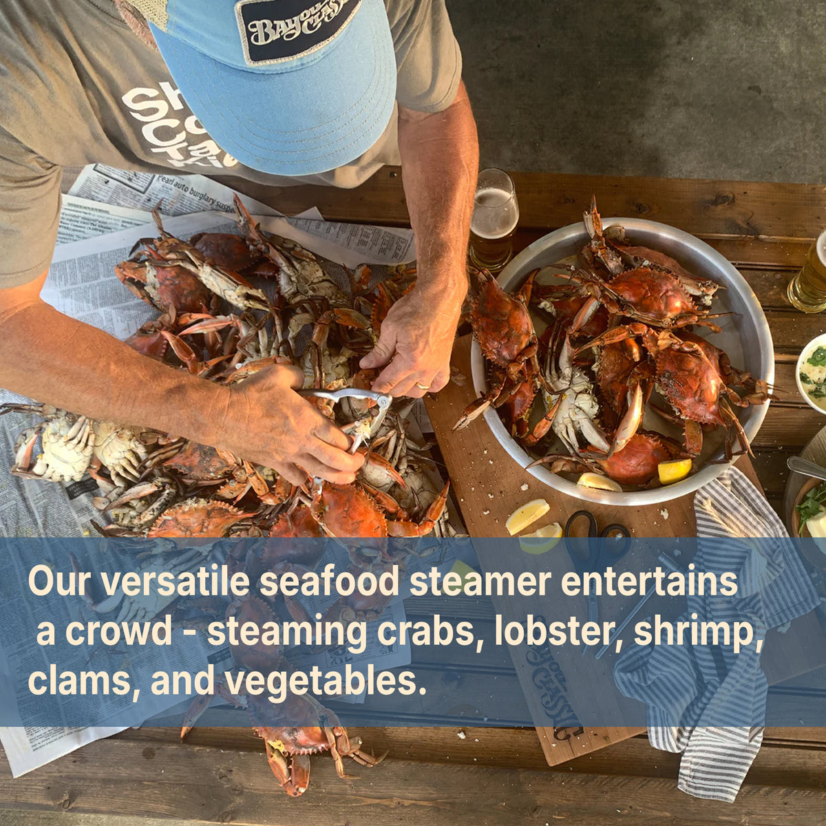 Person cracking crabs on a table and text that reads our versatile seafood steamer entertains a crowd - steaming crabs, lobster, shrimp, clams, and vegetables