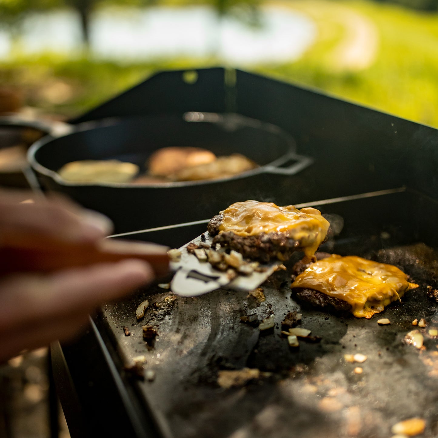 Person cooking burgers on a griddle outdoors