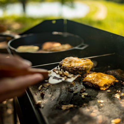 Person cooking burgers on a griddle outdoors