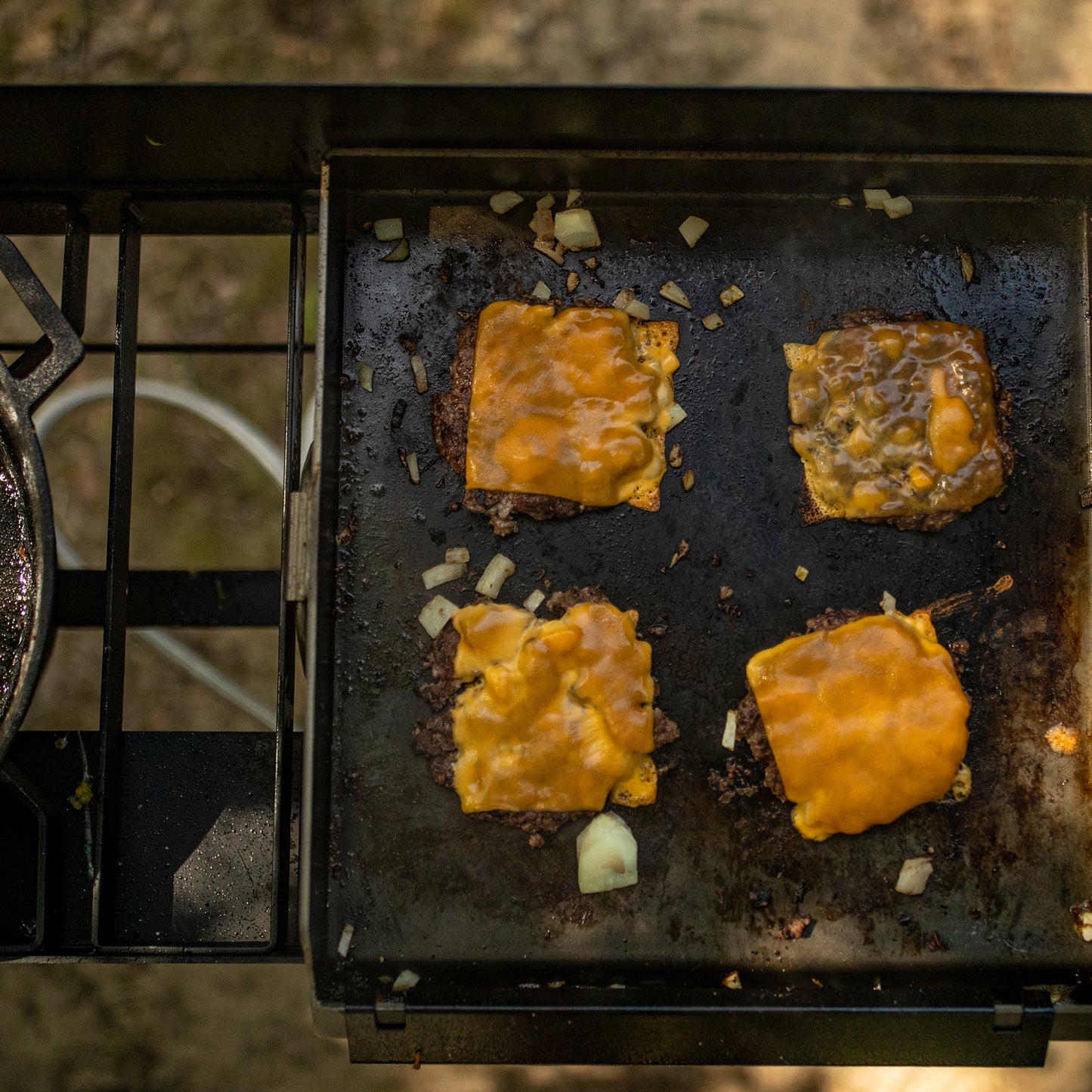 Cheeseburgers cooking on a griddle with melted cheese