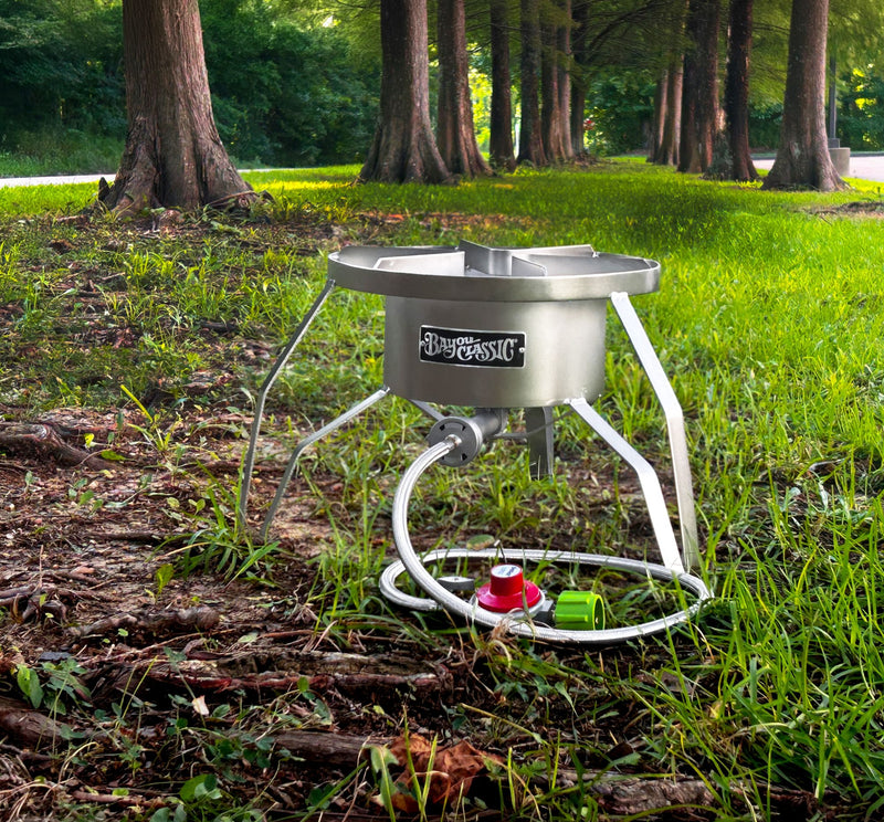 A stainless outdoor cooker set in the grass with a row of trees.