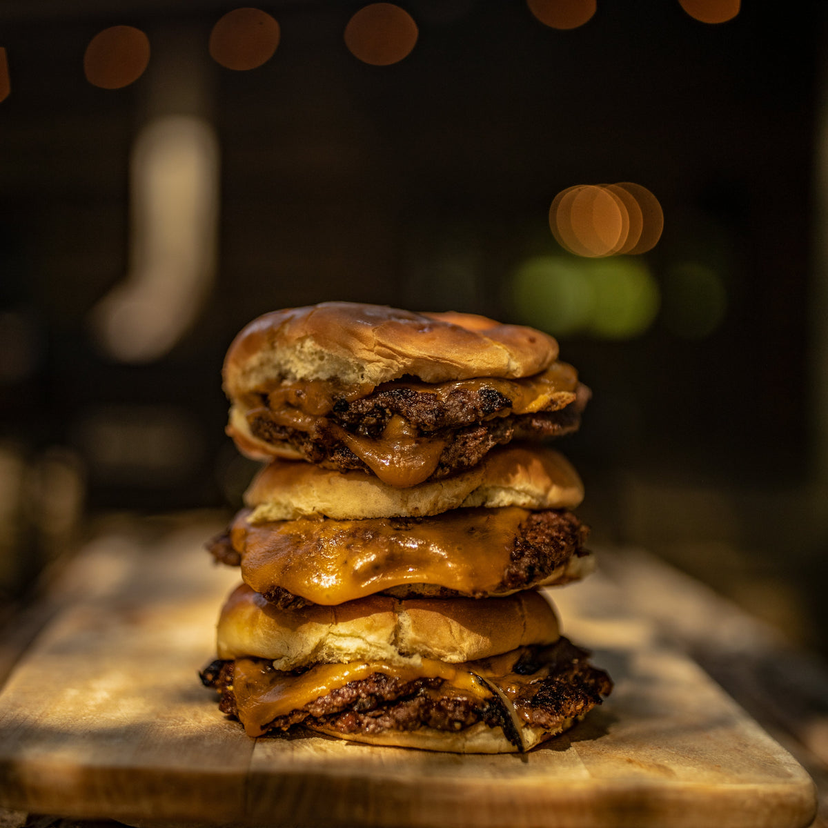 A stack of three smashburgers on a wood table in an outdoor setting