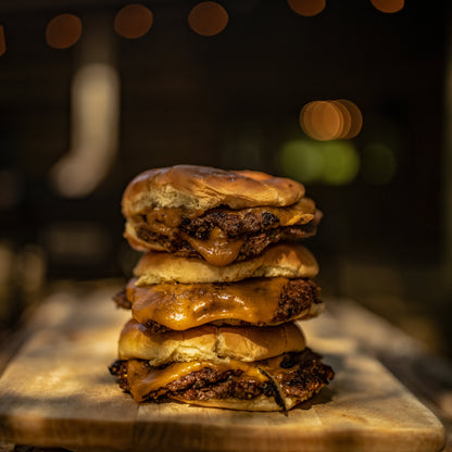 A stack of three smashburgers on a wood table in an outdoor setting