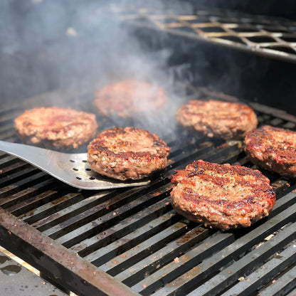 Spatula flipping hamburgers cooking on a grill with smoke