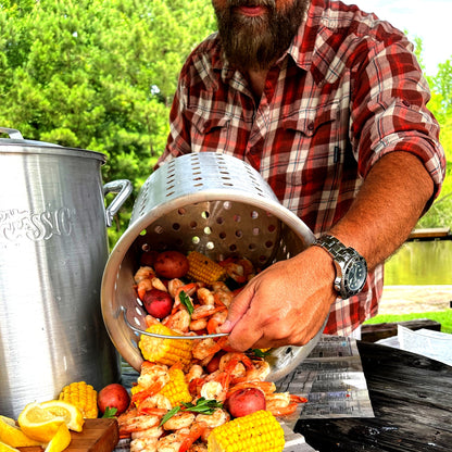 Man pouring a low country boil out of an aluminum basket outside on a table.