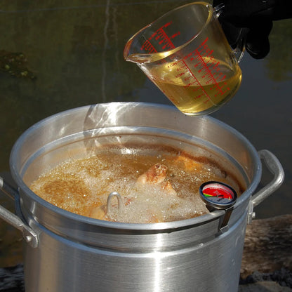 Measuring cup pouring liquid into a turkey fryer that is frying a turkey outside