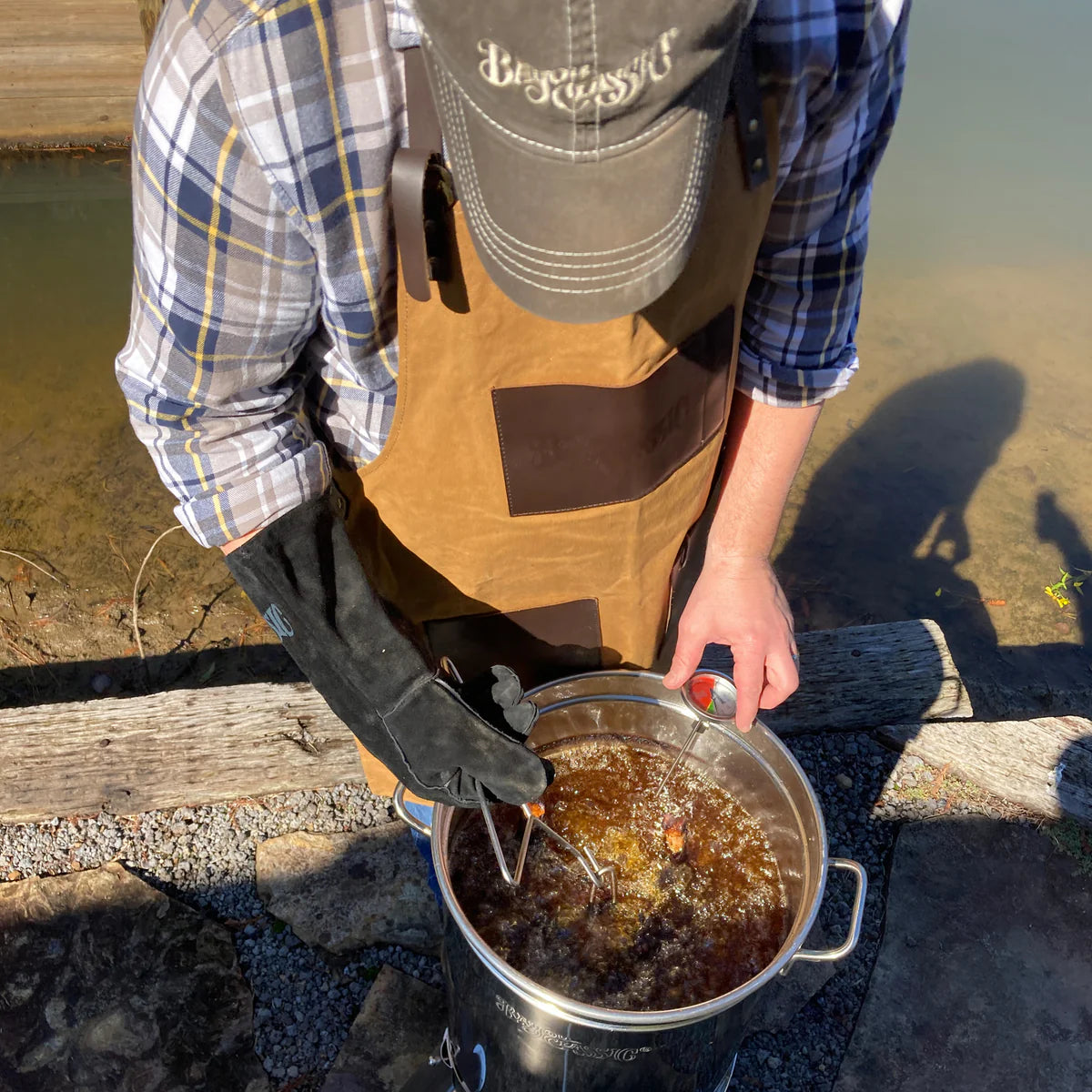 Person frying a turkey in a turkey fryer pot and cooker by a body of water