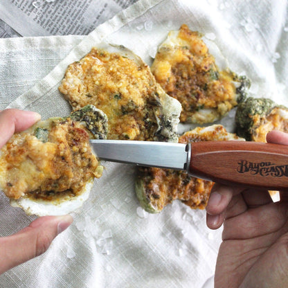 Person using an oyster shucker knife to remove a chargrilled oyster from the shell