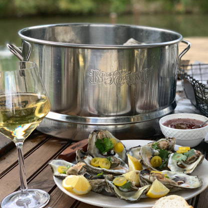 Top of stainless oyster steamer on a table with a plate of steamed oysters and a glass of whit wine