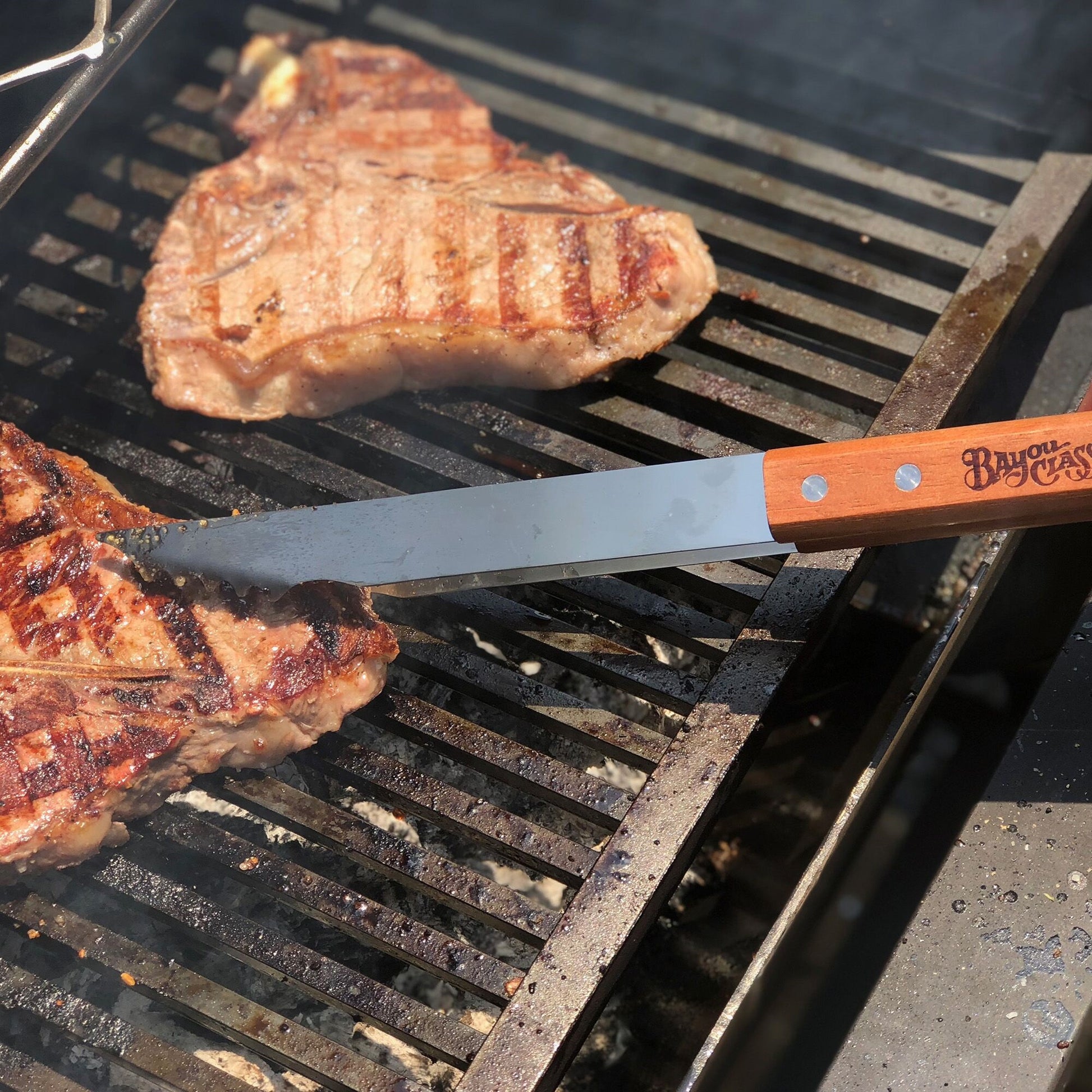 Stainless tongs flipping steaks on a grill