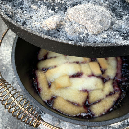Cast Iron Pot with coals on the lid and a berry cobbler cooking