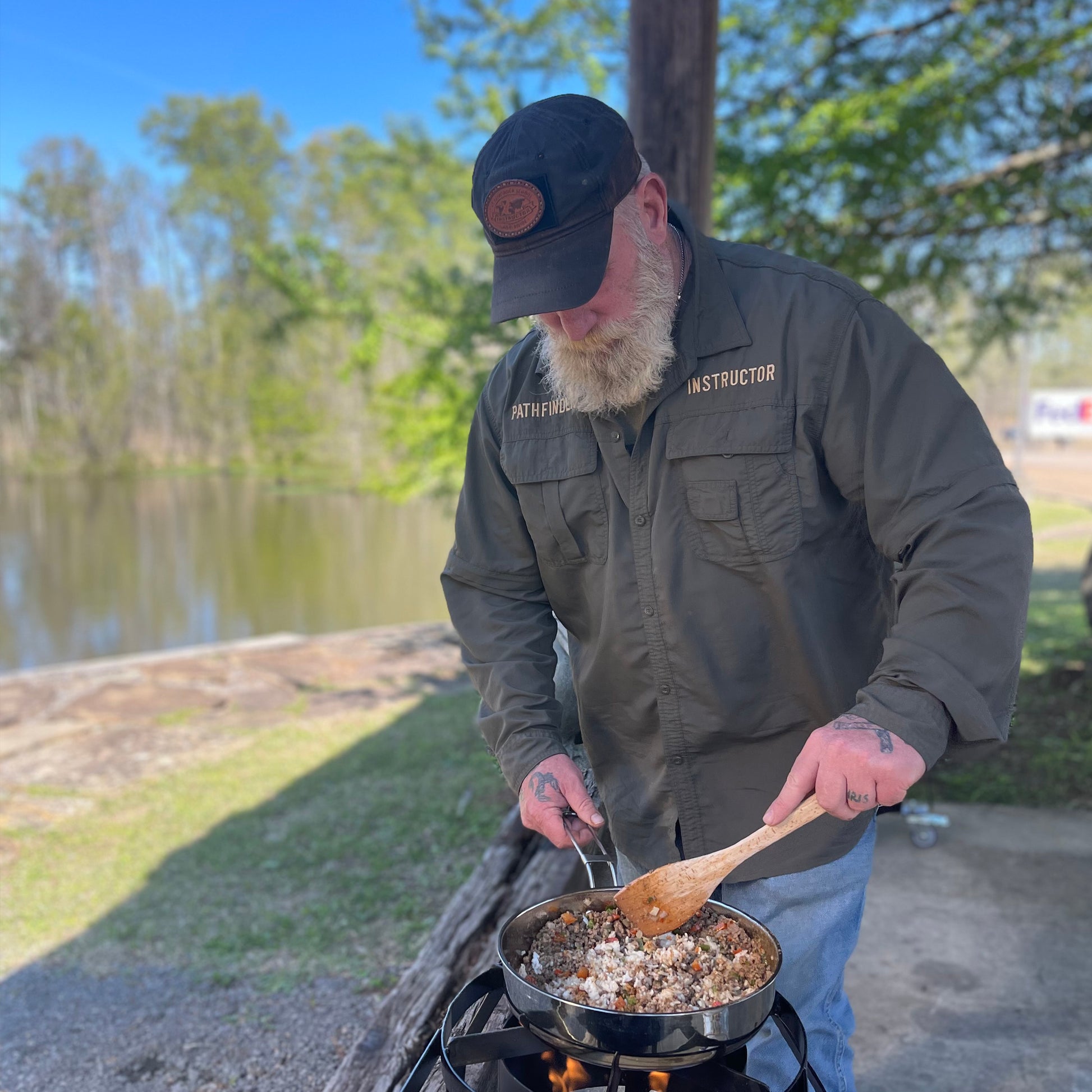 Man cooking with a stainless skillet outside using a propane cooker