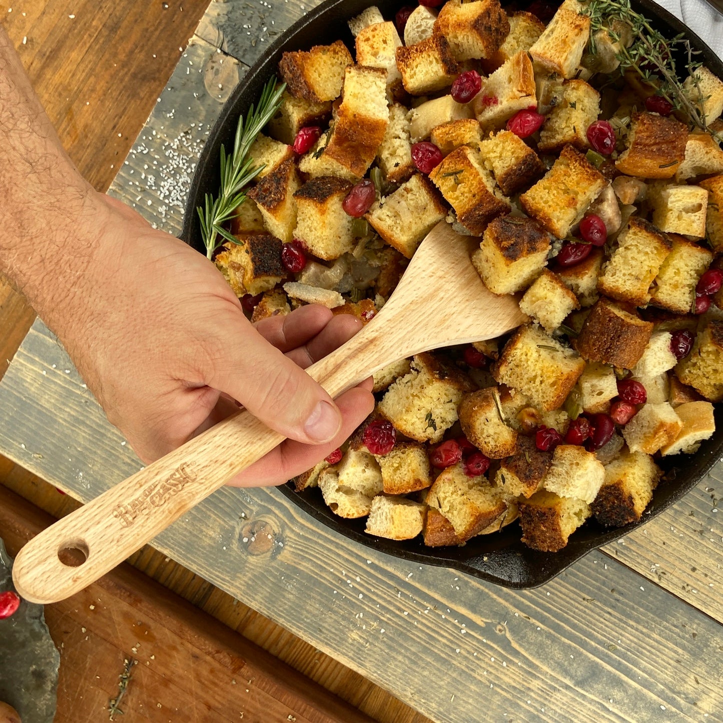 Person holding a wood spoon stirring cornbread dressing in a cast iron skillet